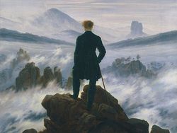 Mann in schwarzem Anzug steht auf einem Felsen, blickt auf eine neblige Landschaft mit Bergen und Wolken.