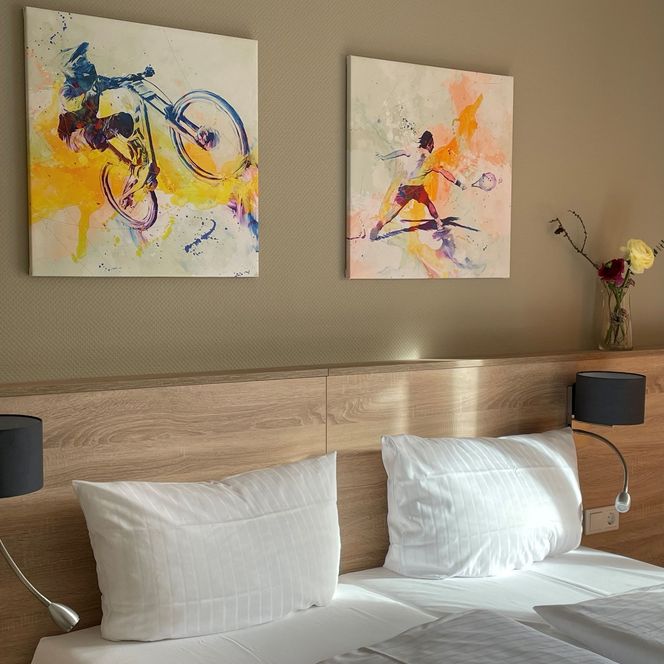 Zwei Bilder an der Wand über einem Bett mit weißen Kissen und einer Holzablage.