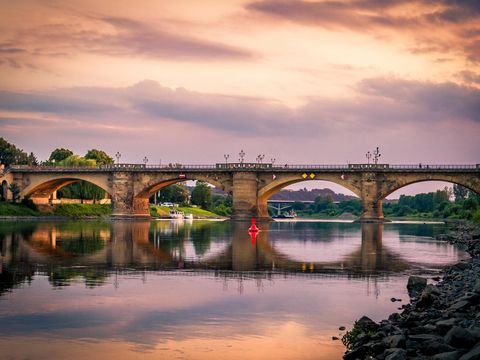 Bogenbrücke über der Elbe, im Hintergrund Häuser und abendroter Himmel.