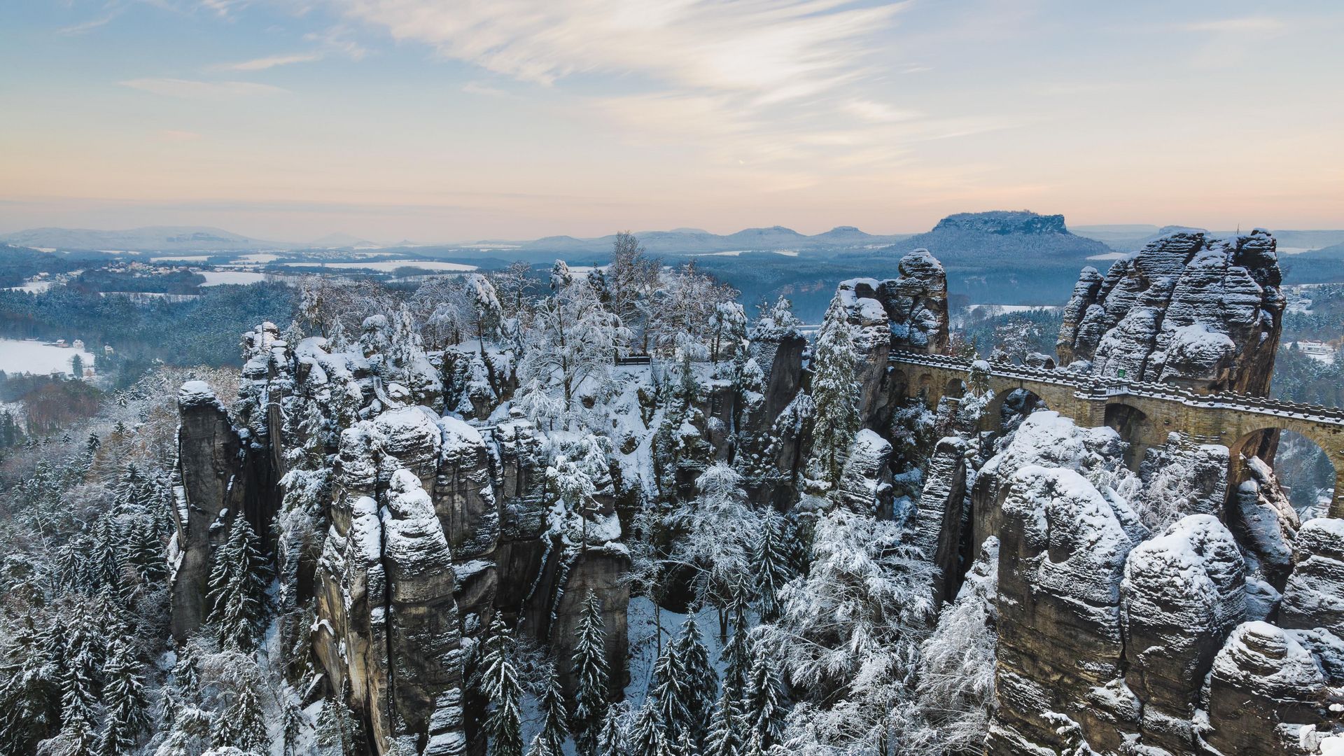 Winterlandschaft mit schneebedeckter Basteibrücke und Felsen.