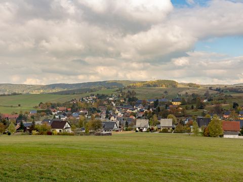 Blick auf Hinterhermsdorf, im Vordergrund grüne Wiesen, bewölkter blauen Himmel.