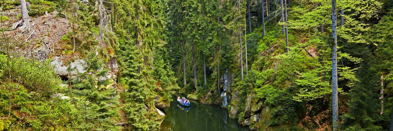 Grüne Bäume umgeben einen schmalen Fluss in einer tiefen Schlucht. Im Hintergrund ist ein Boot zu erkennen.