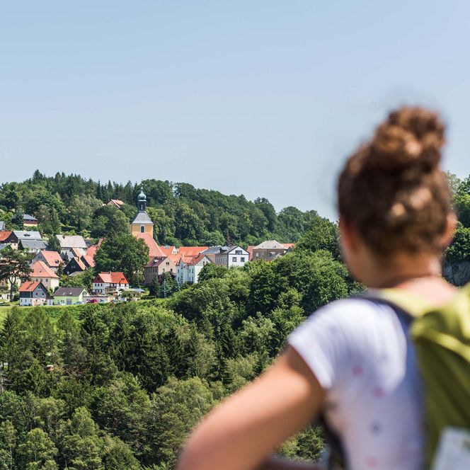 Frau mit Rucksack blickt von der Hockstein-Aussicht auf die Stadt Hohnstein.