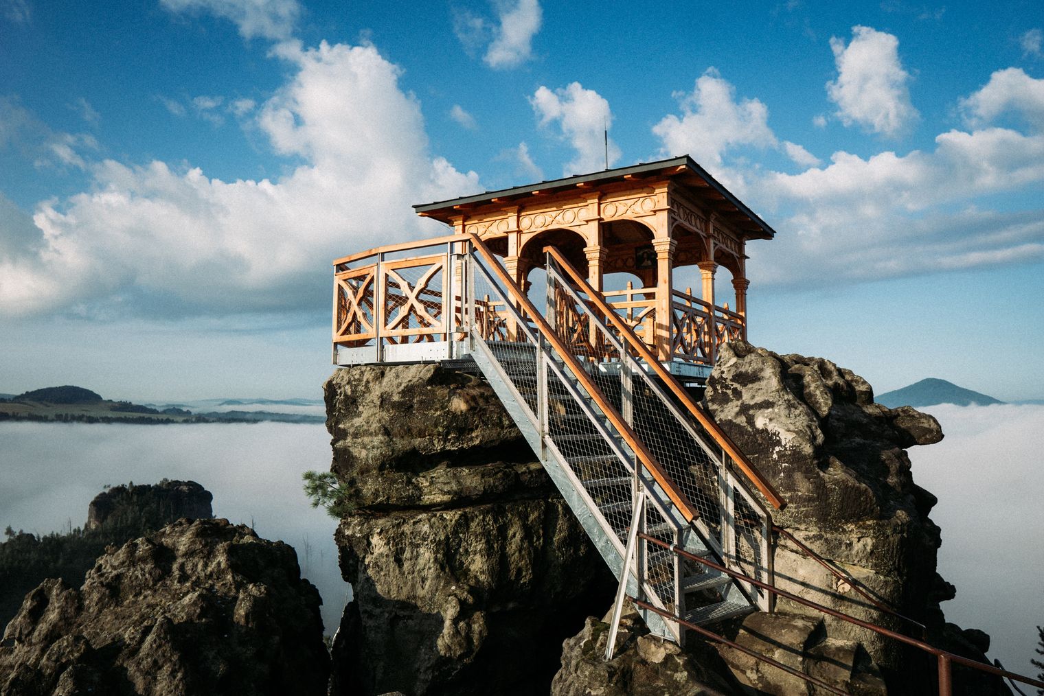 Holzpavillon auf einer Felsformation mit Treppe, umgeben von einem Nebelmeer.