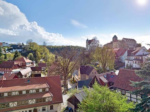 Burg Hohnstein auf einem Hügel, umgeben von Fachwerkhäusern und blauer Himmel im Hintergrund.