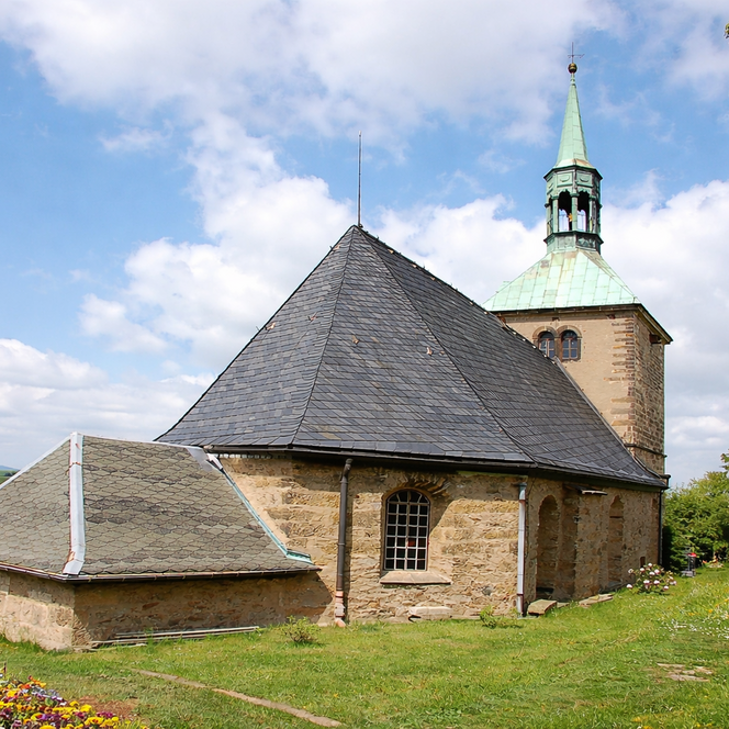 Kleine Kirche mit einem spitzen Dach und einer grünen Kuppel unter einem blauen Himmel.