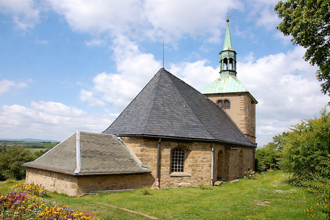 Kleine Kirche mit einem spitzen Dach und einer grünen Kuppel unter einem blauen Himmel.