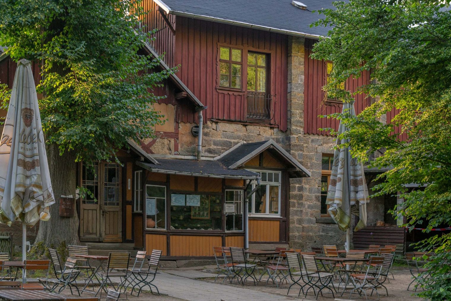 Gemütliche Bergbaude mit Holzfassade, Sonnenschirmen und Sitzgelegenheiten im Freien, umgeben von Bäumen.