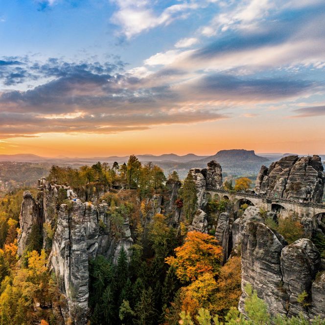 Sonnenuntergang über einer felsigen Landschaft mit Bäumen und weitem Blick ins Tal.