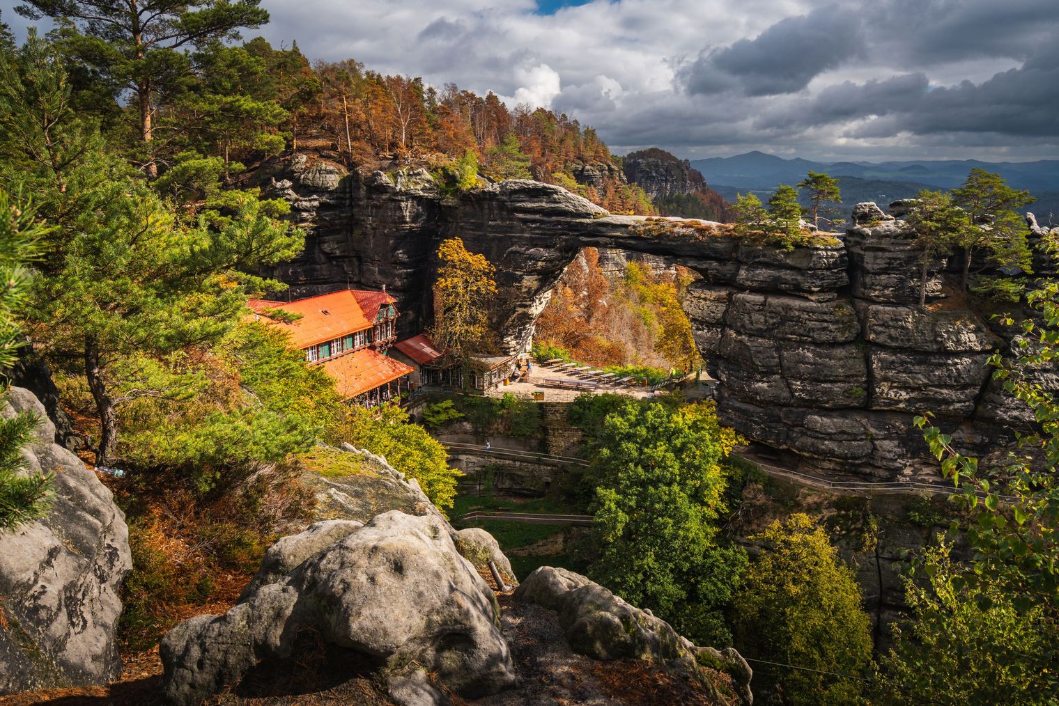 Felsenlandschaft mit einer Brücke, umgeben von Bäumen und bewölktem Himmel.