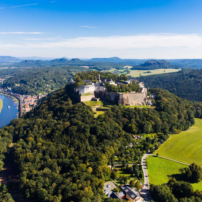 Luftaufnahme einer Burg auf einem Hügel, umgeben von Wäldern und einem Fluss.