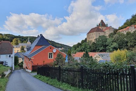 Bunte Häuser und eine Burg auf einem Hügel unter einem blauen Himmel mit Wolken.