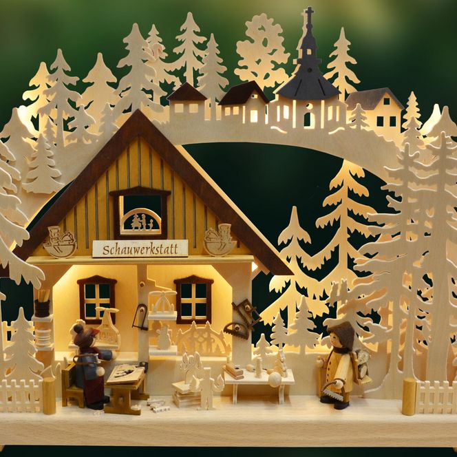 Holzhäuschen mit Weihnachtsdekoration, umgeben von weißen Tannenbäumen und Figuren am Tisch.