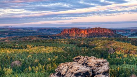 Blick auf eine grüne Landschaft mit Felsen und einem Berg im Hintergrund unter einem bewölkten Himmel.