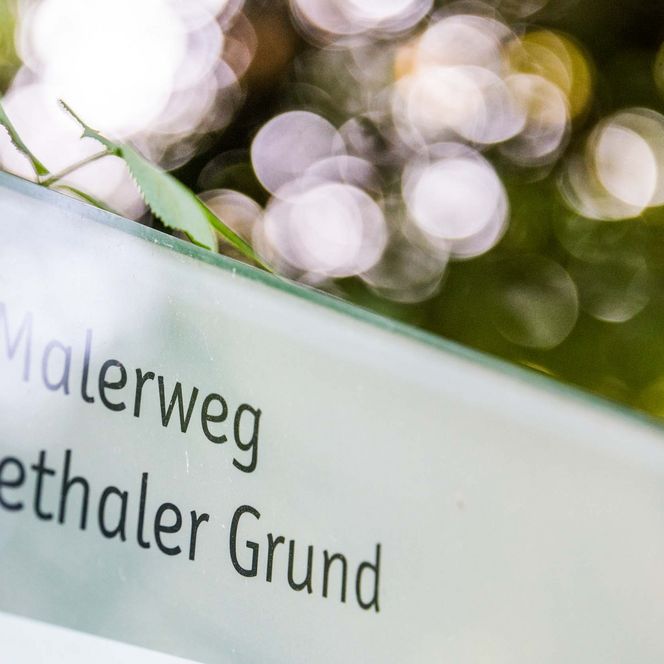 Stele mit der Aufschrift "Liebethaler Grund" vor unscharfem, grünem Hintergrund.