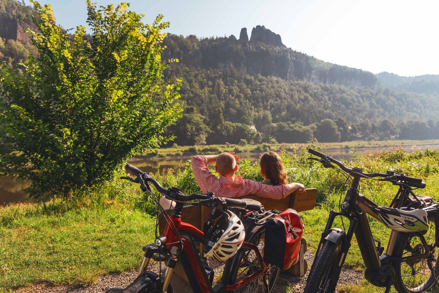 Vier Personen posieren mit Fahrrädern in einer grünen Landschaft, im Hintergrund Berge und Bäume.
