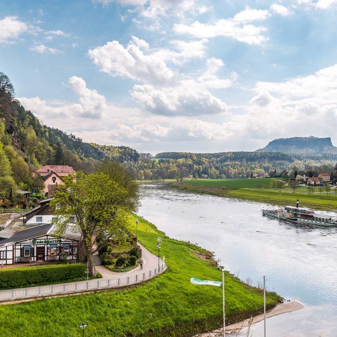 Flusslandschaft mit einem Dampfschiff, umgeben von grünen Hügeln und Häusern am Ufer.