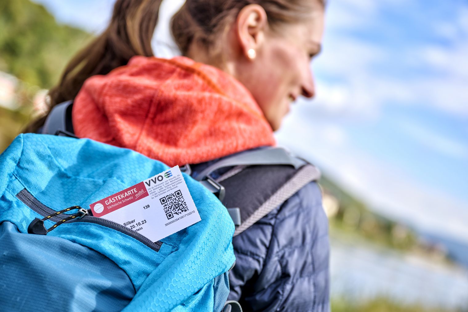 Frau mit Wanderrucksack zeigt die Gästekarte Sächsische Schweiz mobil