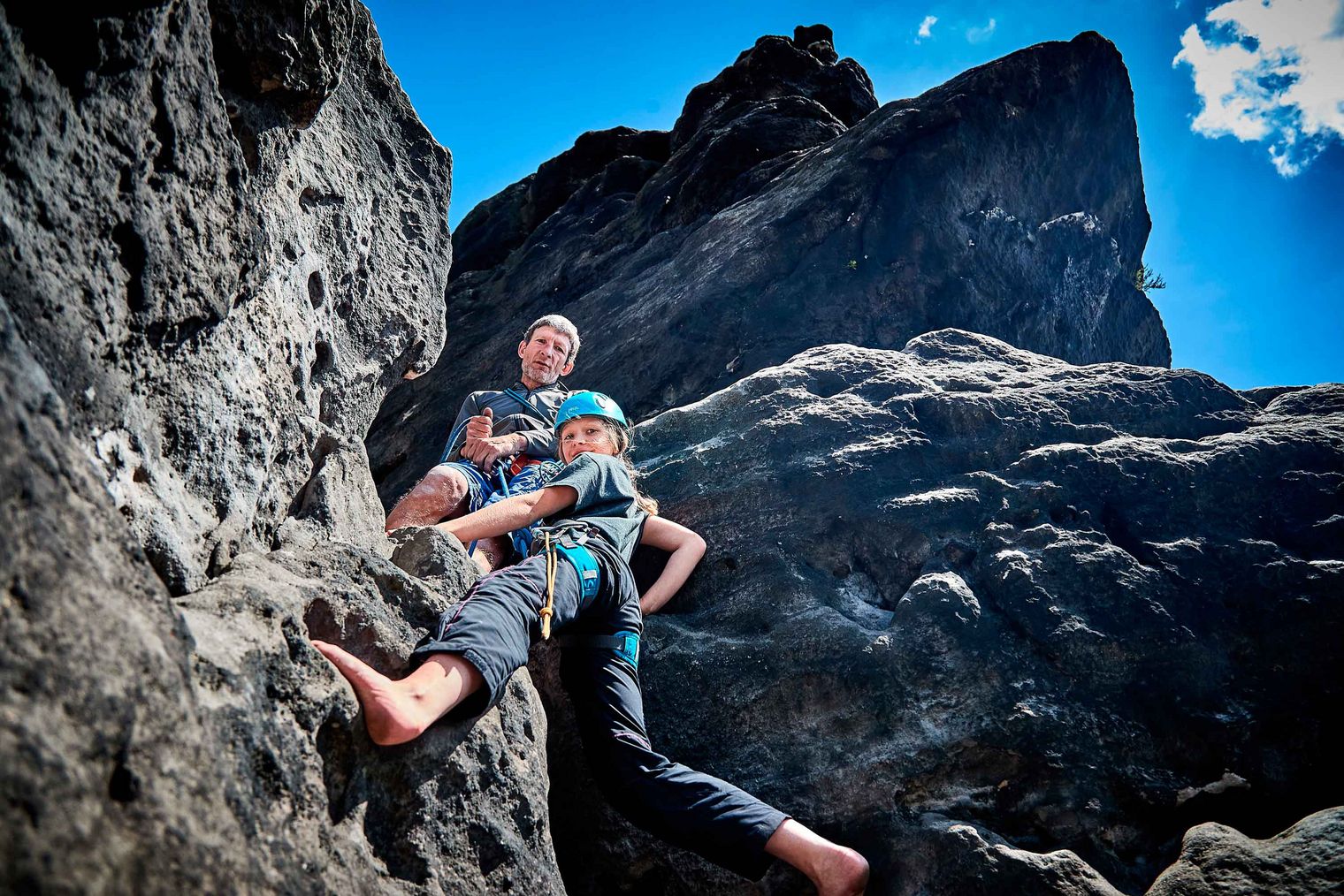 Zwei Personen klettern an einer Felswand unter blauem Himmel.