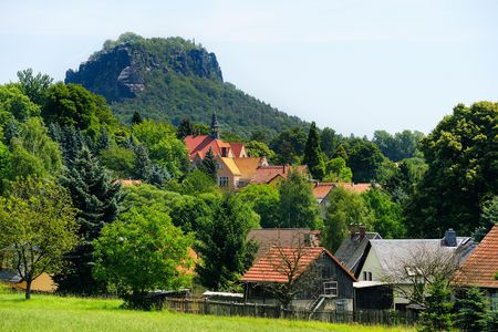Grüne Landschaft mit einem Dorf und einem markanten Berg im Hintergrund.