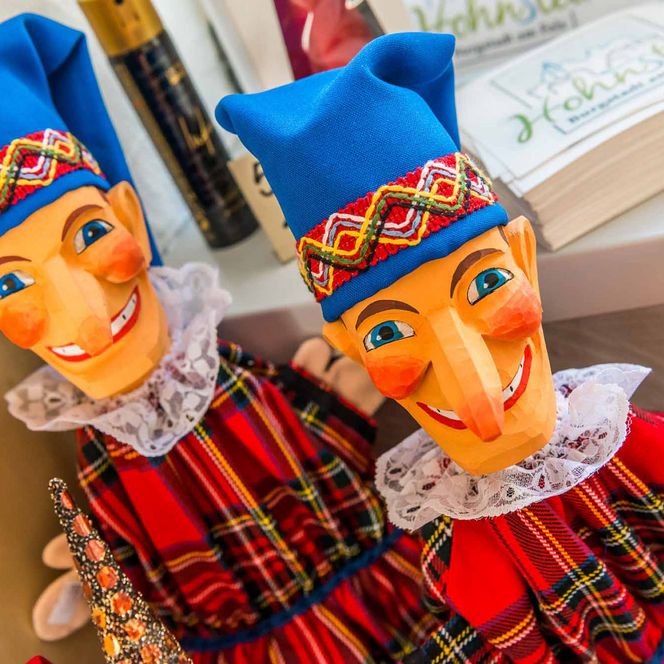 Zwei bunte Holzpuppen des Original Hohnsteiner Kasper mit blauen Mützen und karierten Kleidern, lächeln freundlich.