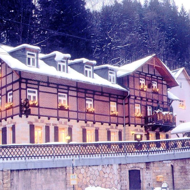 Historisches Gebäude im Winter, mit Holzverkleidung und Schnee bedeckt, umgeben von Tannenbäumen.