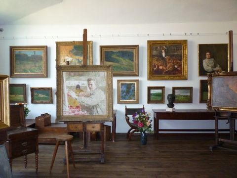 Robert Sterl Haus Struppen Atelier: Atelier mit Holzboden, großen Fenstern, Staffelei, Gemälden und einem Klavier.
