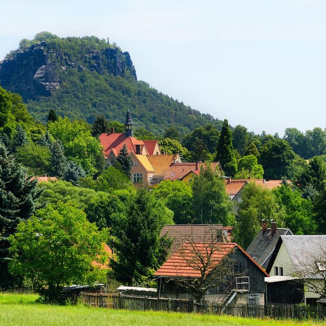 Grüne Landschaft mit einem Dorf und einem markanten Berg im Hintergrund.