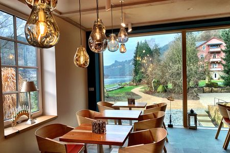 Helle, moderne Café-Atmosphäre mit Holzstühlen, Tischen und großen Fenstern zum Garten.