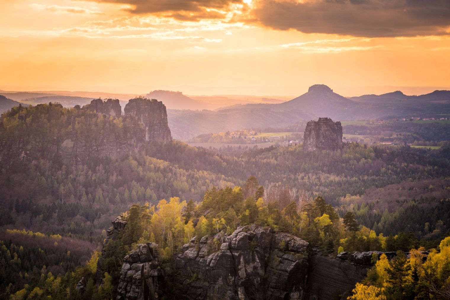 Sonnenuntergang über einer hügeligen Landschaft mit Felsen und Bäumen im Vordergrund.