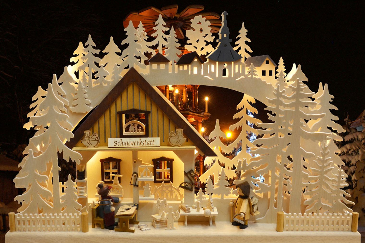 Weihnachtliche Szene mit einem Holzhaus, umgeben von weißen Tannenbäumen und festlicher Beleuchtung.