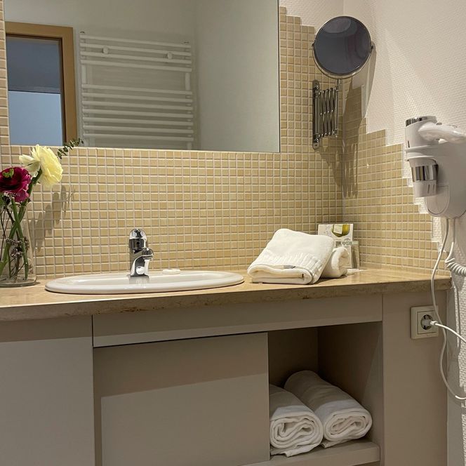 Badezimmer mit Waschbecken, Handtuchhalter und Fön an der Wand.