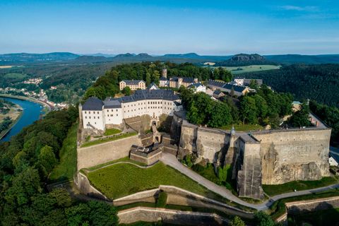 Luftaufnahme der Festung Königstein, umgeben von grünen Wäldern und dem Fluss Elbe im Hintergrund.