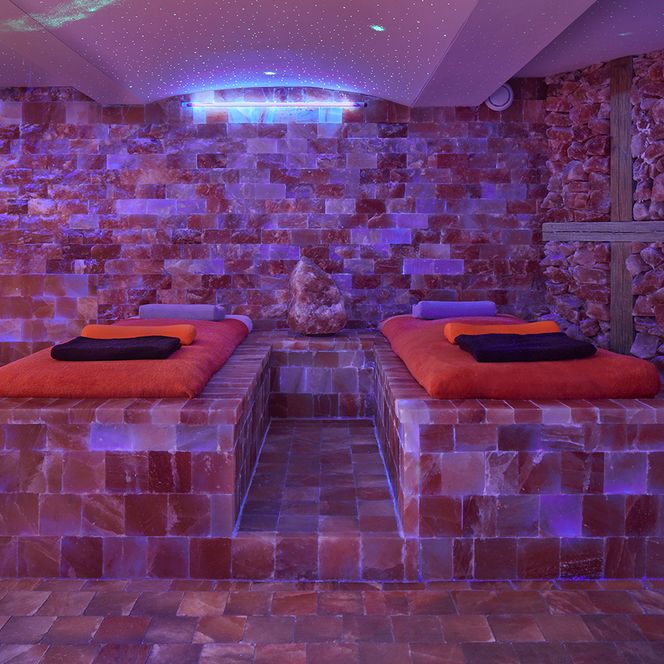 Ruhiger Wellnessbereich mit bunten Lichtern, Steinwänden und zwei roten Liegen.