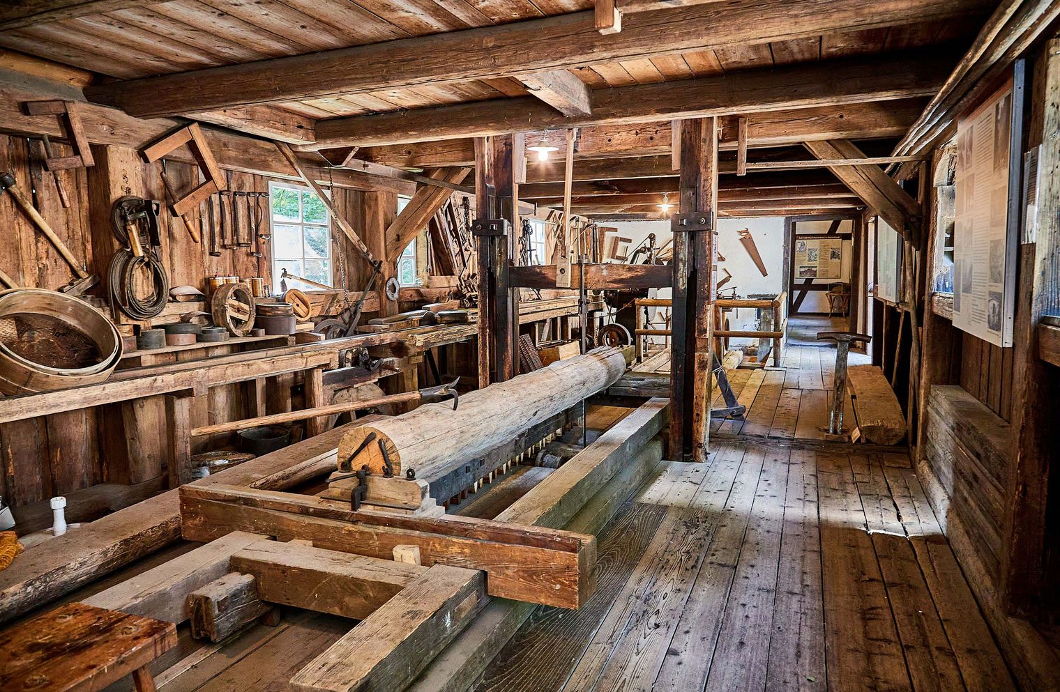 Museumsraum der Neumannmühle mit Holzwerkstatt mit Maschinen, Holzstämmen und Werkzeugen in einem rustikalen, hölzernen Innenraum.