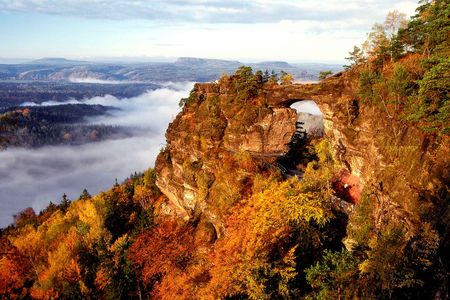 Felsformation mit einem natürlichen Bogen, umgeben von buntem Laub und Nebel in der Ferne.
