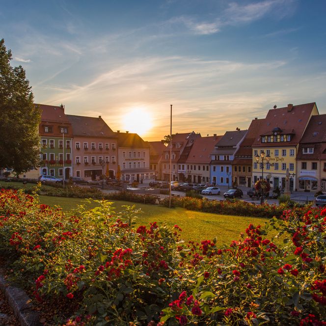 Sonnenuntergang über einem malerischen Stadtplatz mit bunten Blumen und historischen Gebäuden.