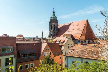 Blick auf ein Stadtbild mit roten Dächern und einem Kirchturm unter blauem Himmel.