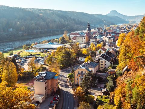 Luftaufnahme von Bad Schandau mit grünen Hügeln, Fluss und Brücke im Vordergrund.