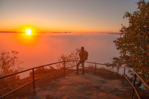 Person steht auf einem Aussichtspunkt und schaut auf einen Sonnenuntergang über dem Nebelmeer des Elbsandsteingebirges.