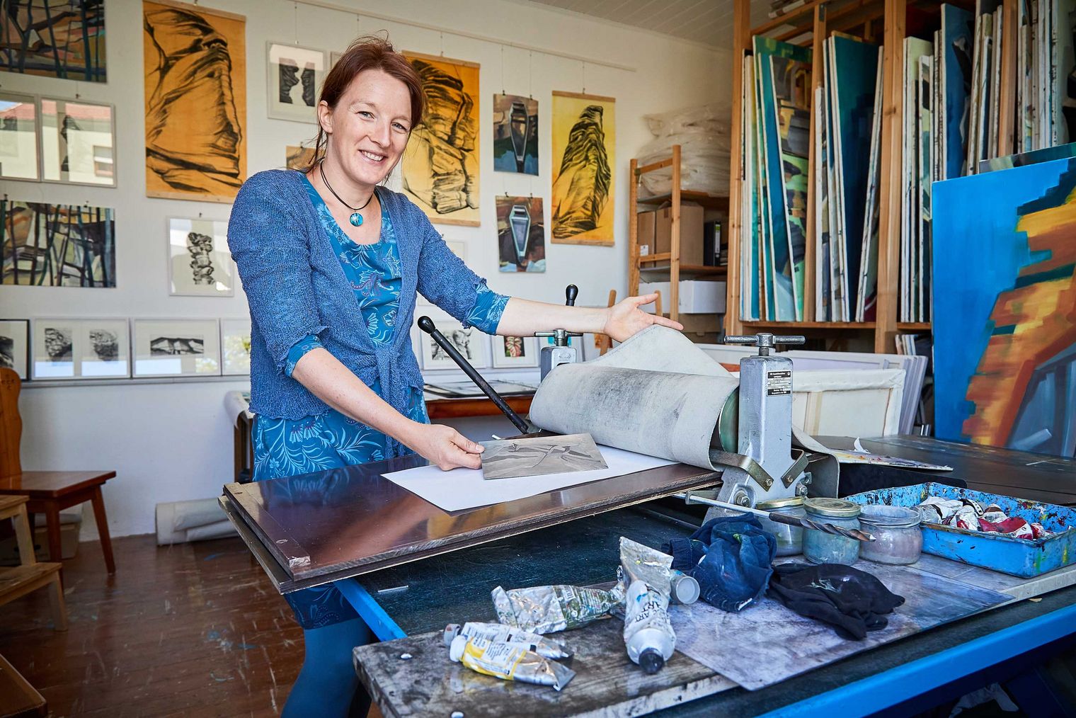 Künstlerin in einem Atelier, die begeistert an einem Tisch mit Kunstmaterialien arbeitet.