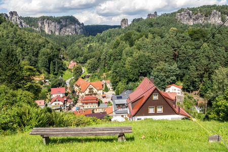 Landschaft mit mehreren roten und weißen Häusern, umgeben von grünen Bäumen und Hügeln.