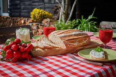 Ein gedeckter Tisch mit rot-weißem Tischdecken, frischem Brot, Erdbeeren, Getränken und einer kleinen Speise.