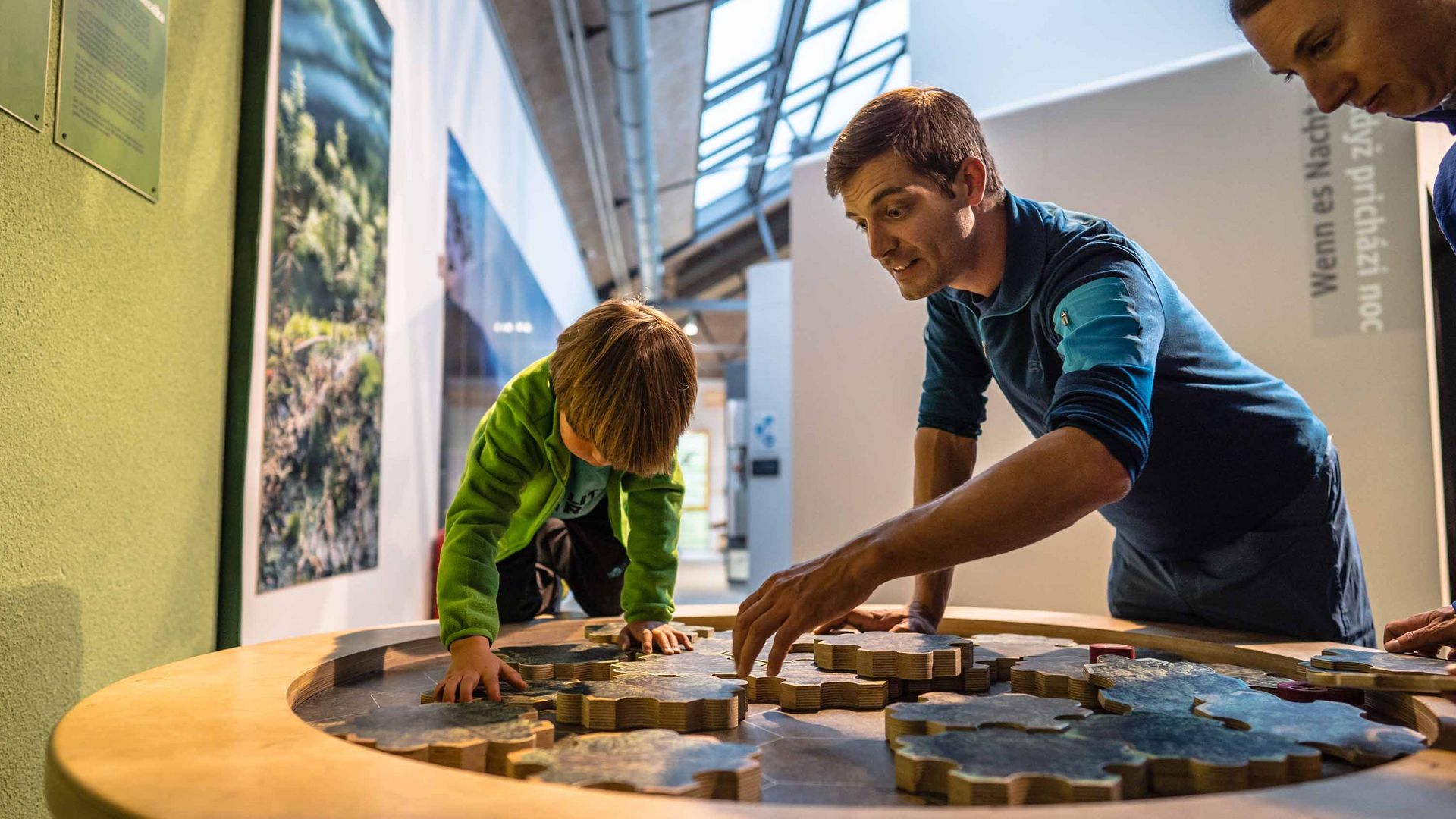 Drei Personen, darunter ein Kind, erkunden gemeinsam eine interaktive Ausstellungstafel.