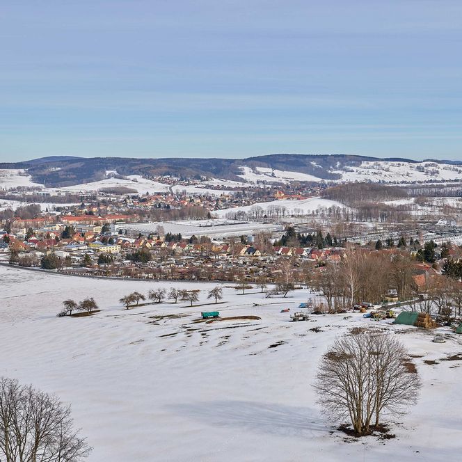 Schneebedeckte Landschaft mit einem Dorf, Bäumen und Bergen im Hintergrund.
