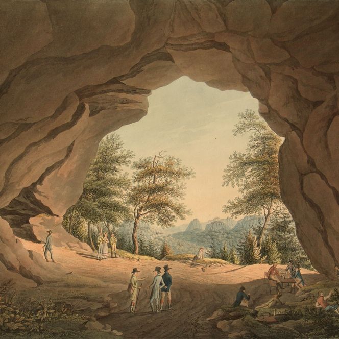 Blick in eine Höhle mit Bäumen und Bergen im Hintergrund; zwei Personen stehen im Vordergrund.