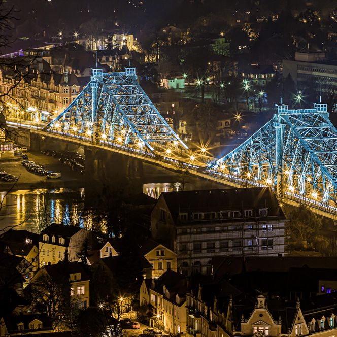 Beleuchtete Brücke mit blauen Lichtern über einem Fluss, umgeben von Stadtlichtern bei Nacht.
