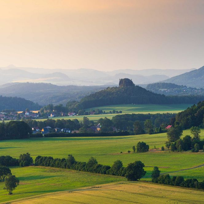 Grüne Landschaft mit sanften Hügeln und dem Rosenberg sowie dem Zirkelstein im Hintergrund unter einem farbenfrohen Himmel.