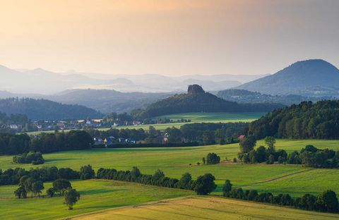Grüne Landschaft mit sanften Hügeln und dem Rosenberg sowie dem Zirkelstein im Hintergrund unter einem farbenfrohen Himmel.