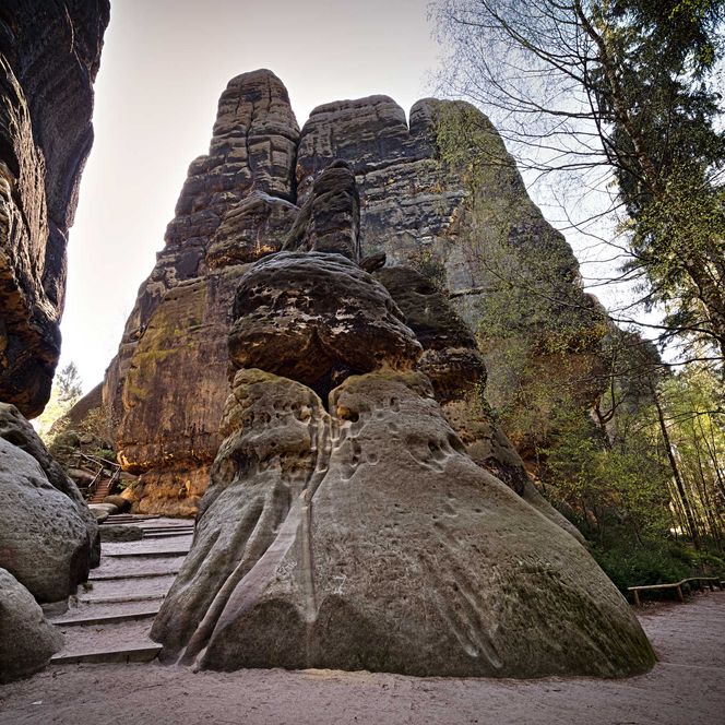 Hohe Felsen umgeben von Bäumen, mit einer Treppe, die zu einer Felsformation führt.